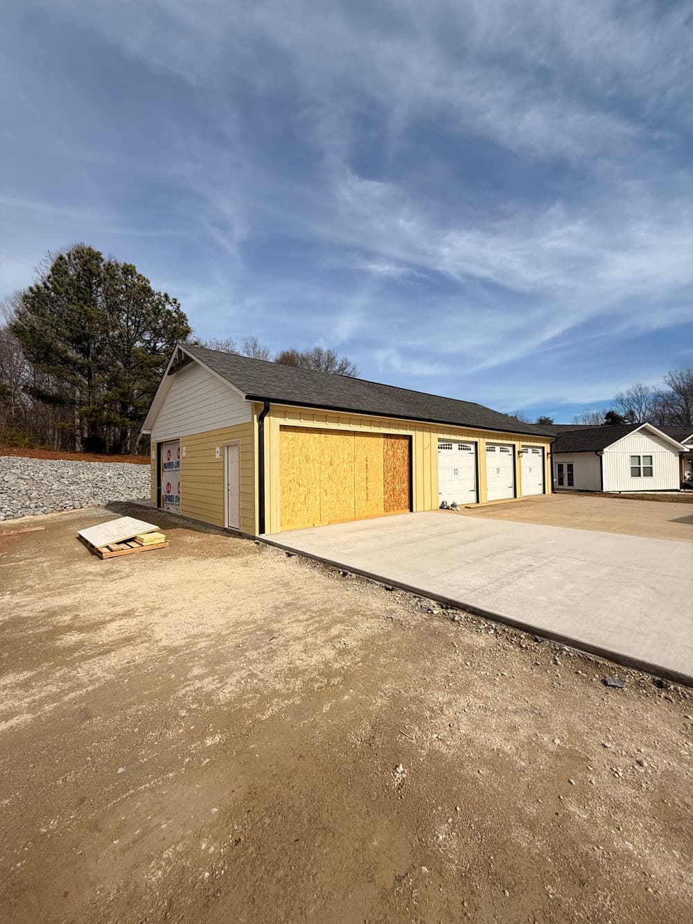 Newly constructed garage with yellow siding and plywood on one door, set against a clear sky.