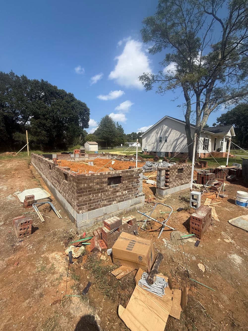 Construction site with brick foundation and tools amidst a residential area.