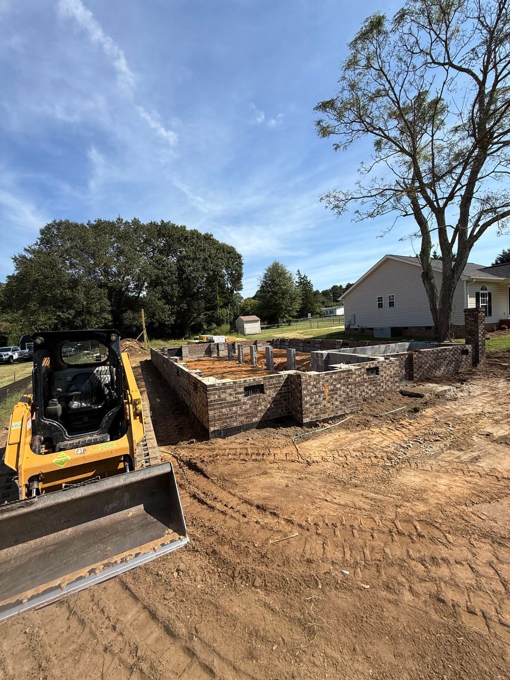Construction site with a bulldozer, new brick foundation, and clear blue sky.