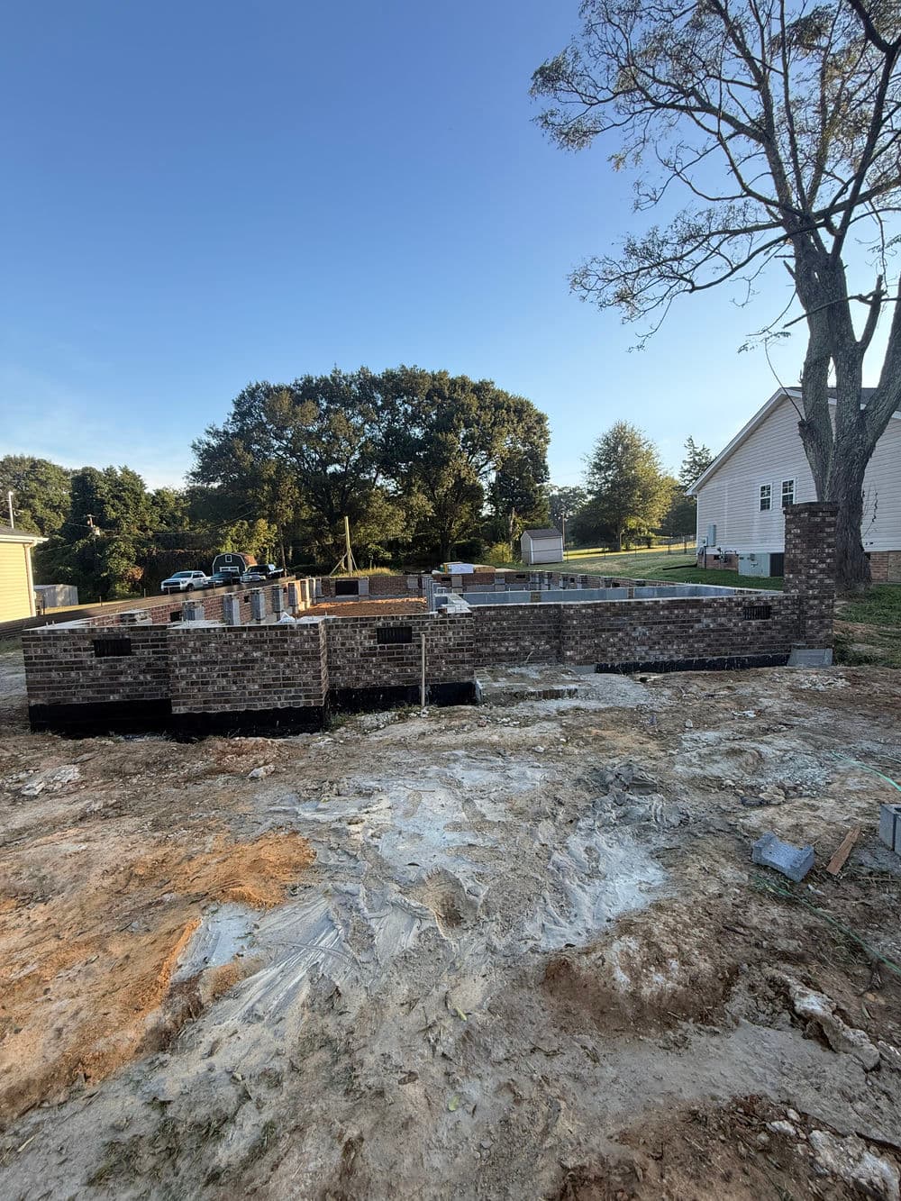 Construction site with brick foundation and trees under clear blue sky.