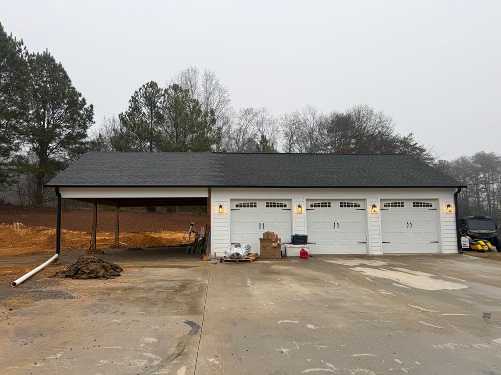 Modern garage with three doors, asphalt driveway, and construction materials nearby.