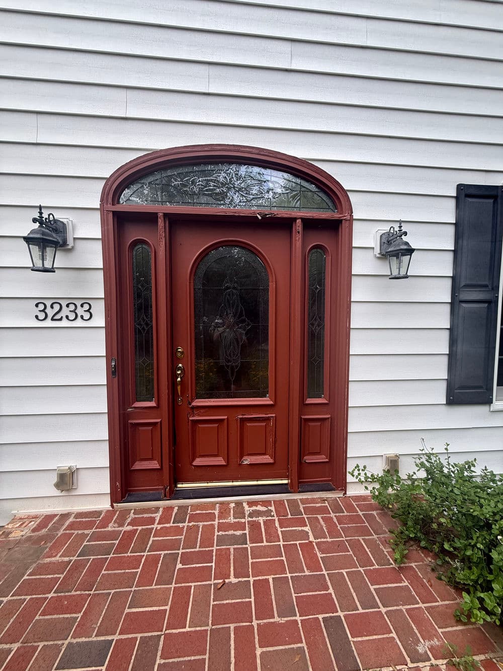 Historic red front door with arched window, flanked by outdoor sconces and brick pathway.