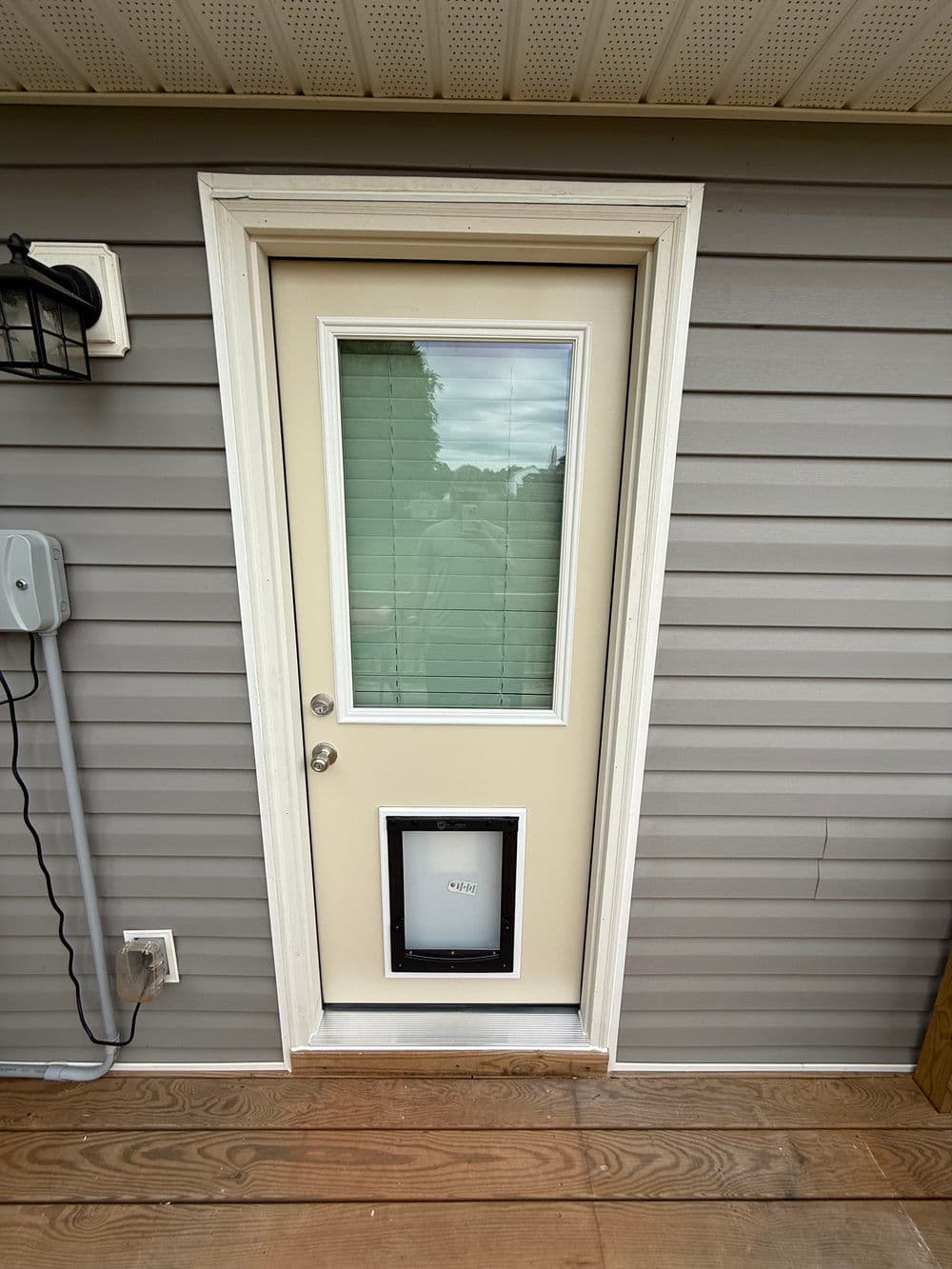 Exterior view of a beige door with a pet door, framed by light gray siding.
