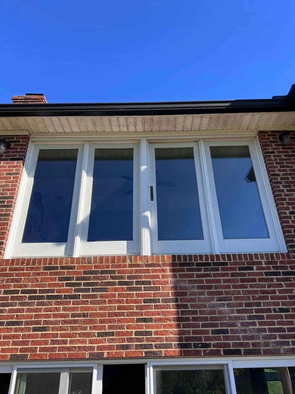 Modern white window on a brick house under a clear blue sky. Bright natural light.