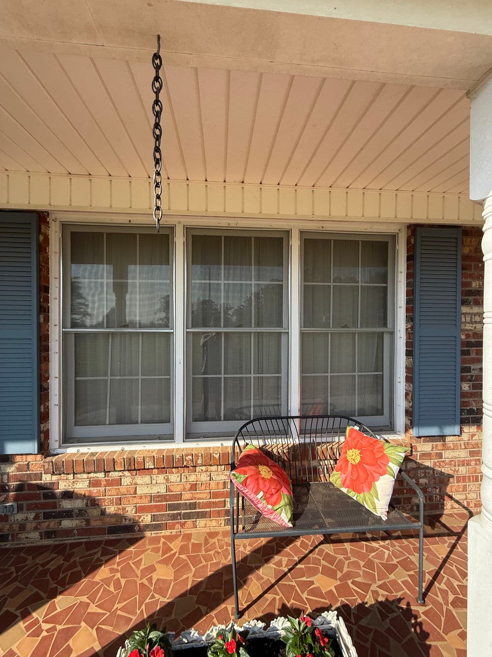 Front porch with a metal bench, colorful cushions, flower box, and brick wall.