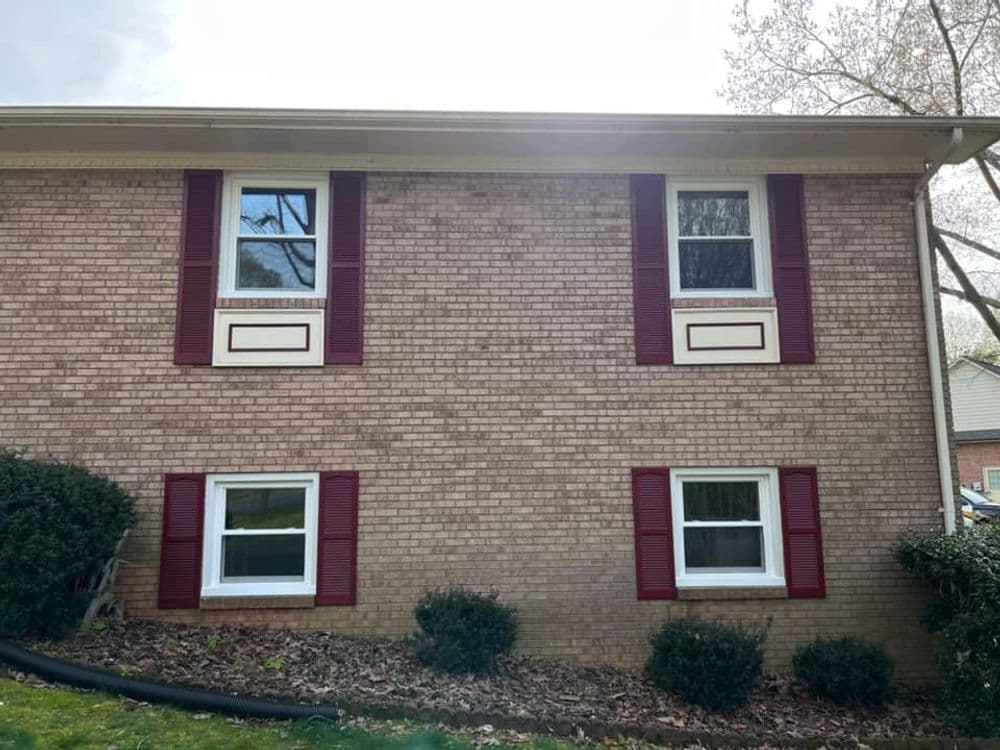 Brick house exterior with red shutters, two windows, and landscaped shrubs.