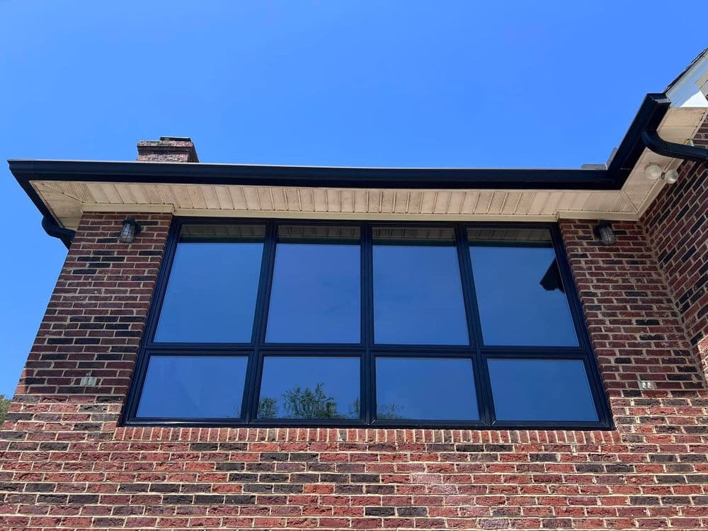 Modern brick house with large black-framed windows against a clear blue sky.