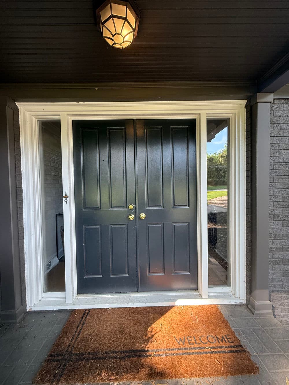 Front entrance with double doors, welcome mat, and decorative light fixture.