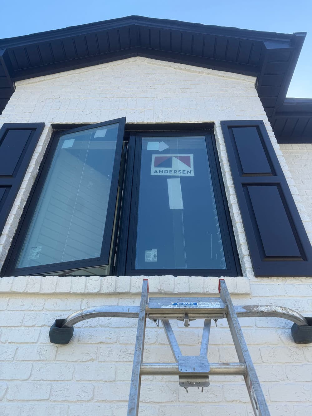 Andersen window installation with ladder in front of a white brick house exterior.