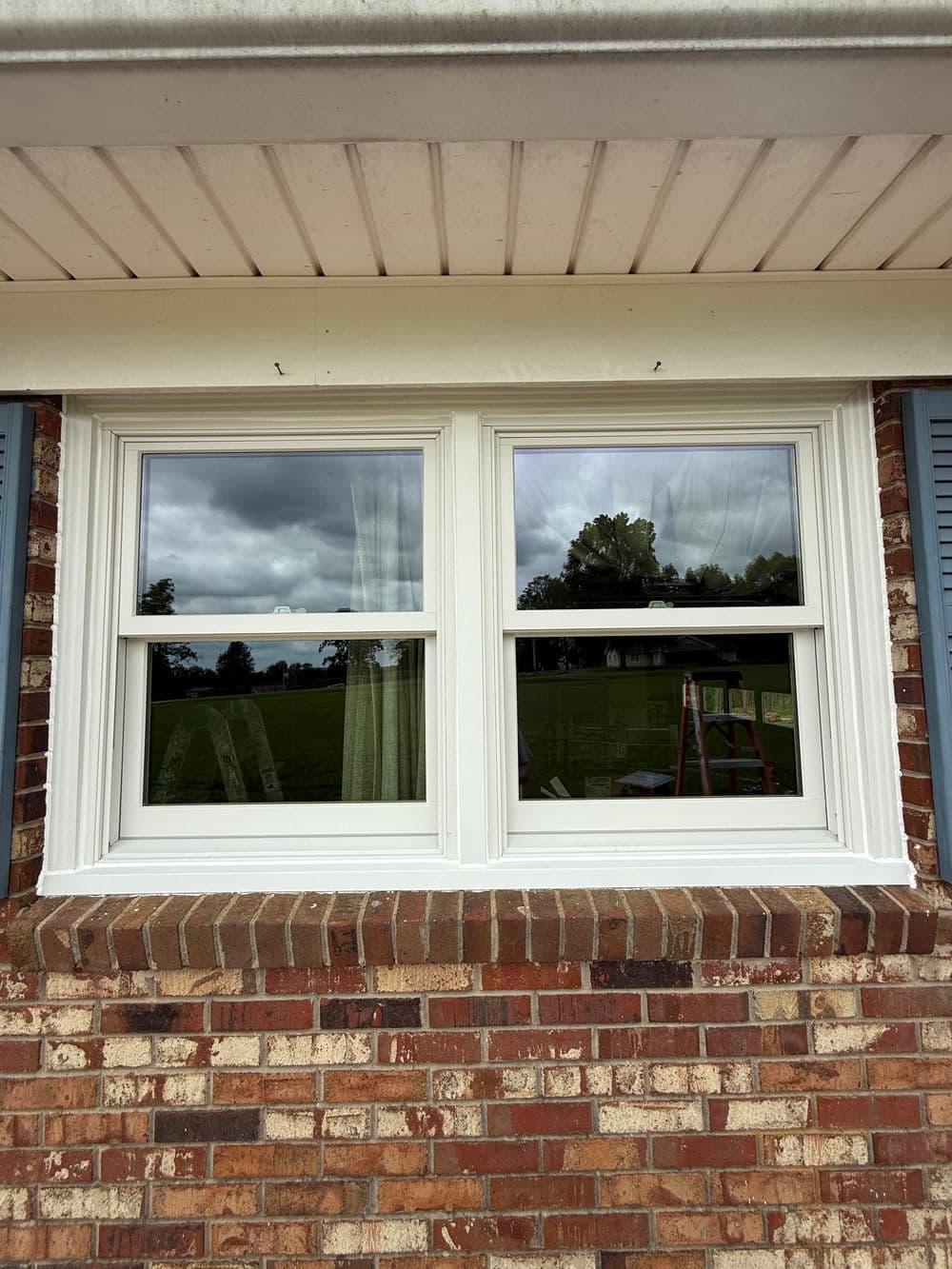 Two white vinyl windows with clear glass set in a brick wall, featuring a cloudy sky backdrop.