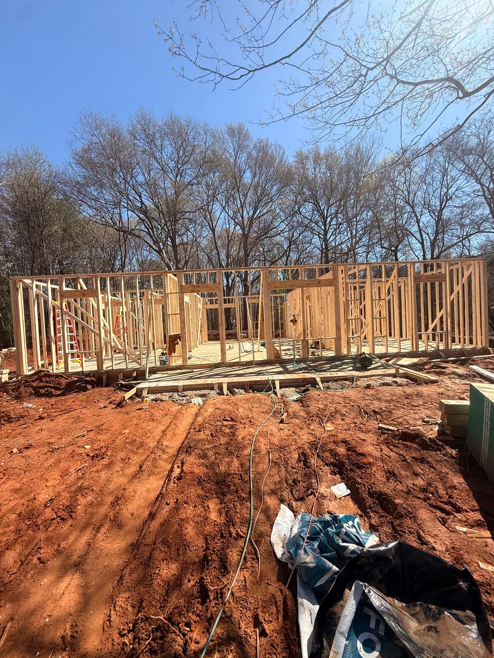New home construction with wooden framing against a blue sky and bare trees.