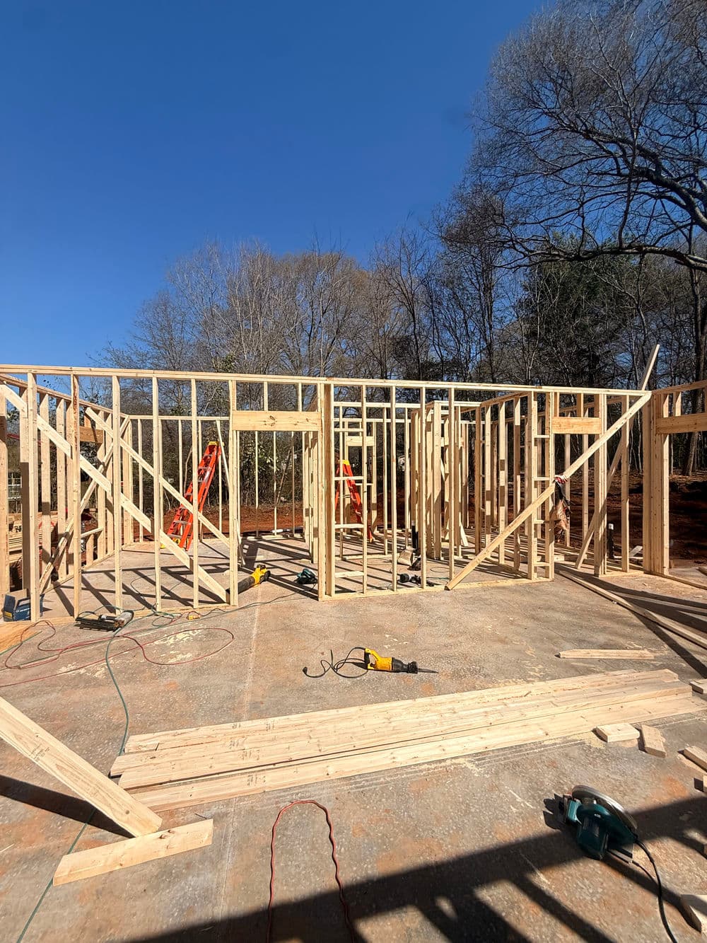 Construction site with wooden framing, tools, and ladders under a clear blue sky.